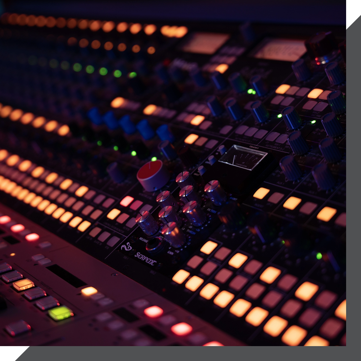 Close-up of a professional audio mixing console in a dimly lit recording studio in London. The console features numerous knobs, buttons, and sliders, all illuminated with various colored lights. The lights create a vibrant, visually striking effect.