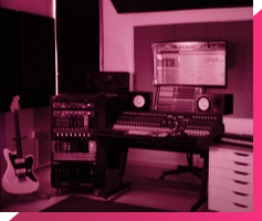 A recording studio in London with a central computer screen displaying audio software, surrounded by speakers, various keyboards, mixers, and six guitars standing in a rack. The room is illuminated with purple and blue lighting, creating a vibrant atmosphere.